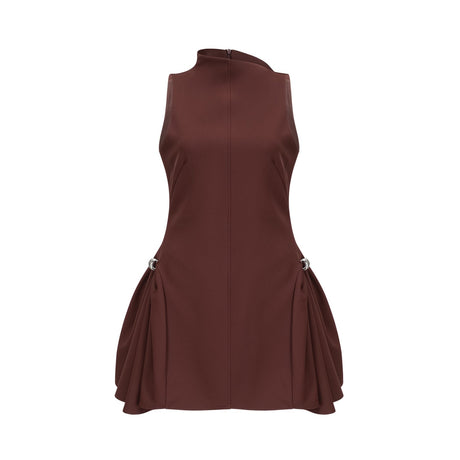 A young woman wearing a short brown dress with an asymmetric neckline and puffed sleeves standing against a plain background