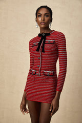 A young woman wearing a short knitted dress with a prominent bow detail standing in a casual pose