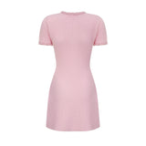 A young woman wearing a short pink knitted dress with beaded embellishments standing against a plain background