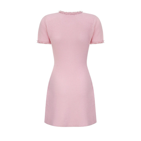 A young woman wearing a short pink knitted dress with beaded embellishments standing against a plain background