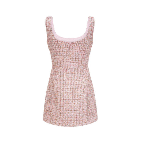 A young woman wearing a short pink tweed dress with sparkly embellishments standing in a casual pose against a plain background