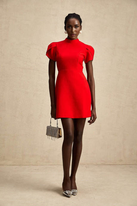 A young woman wearing a short red dress with petal sleeves a cutout design and a bow detail