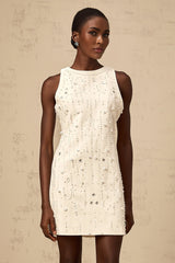 A young woman wearing a short white Aline dress with embellishments standing in a neutral studio setting