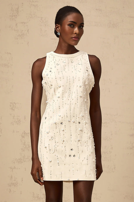 A young woman wearing a short white Aline dress with embellishments standing in a neutral studio setting