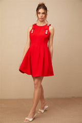 A young woman wearing a sleeveless red mini dress with a pleated skirt and a bow detail at the neckline