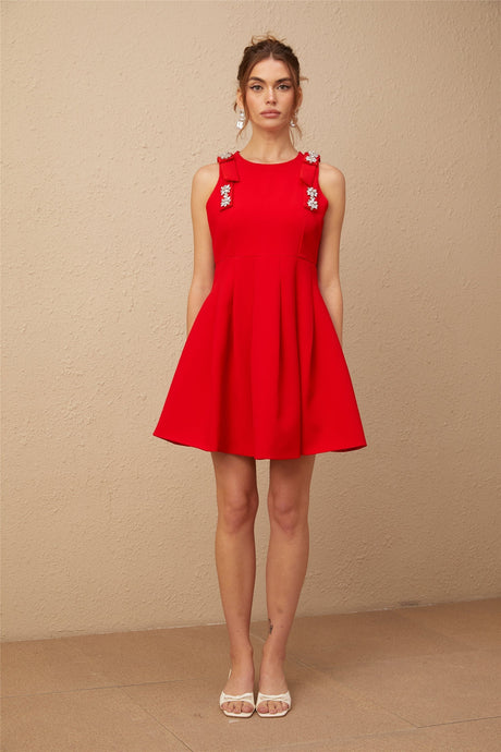 A young woman wearing a sleeveless red mini dress with a pleated skirt and a large bow detail at the neckline