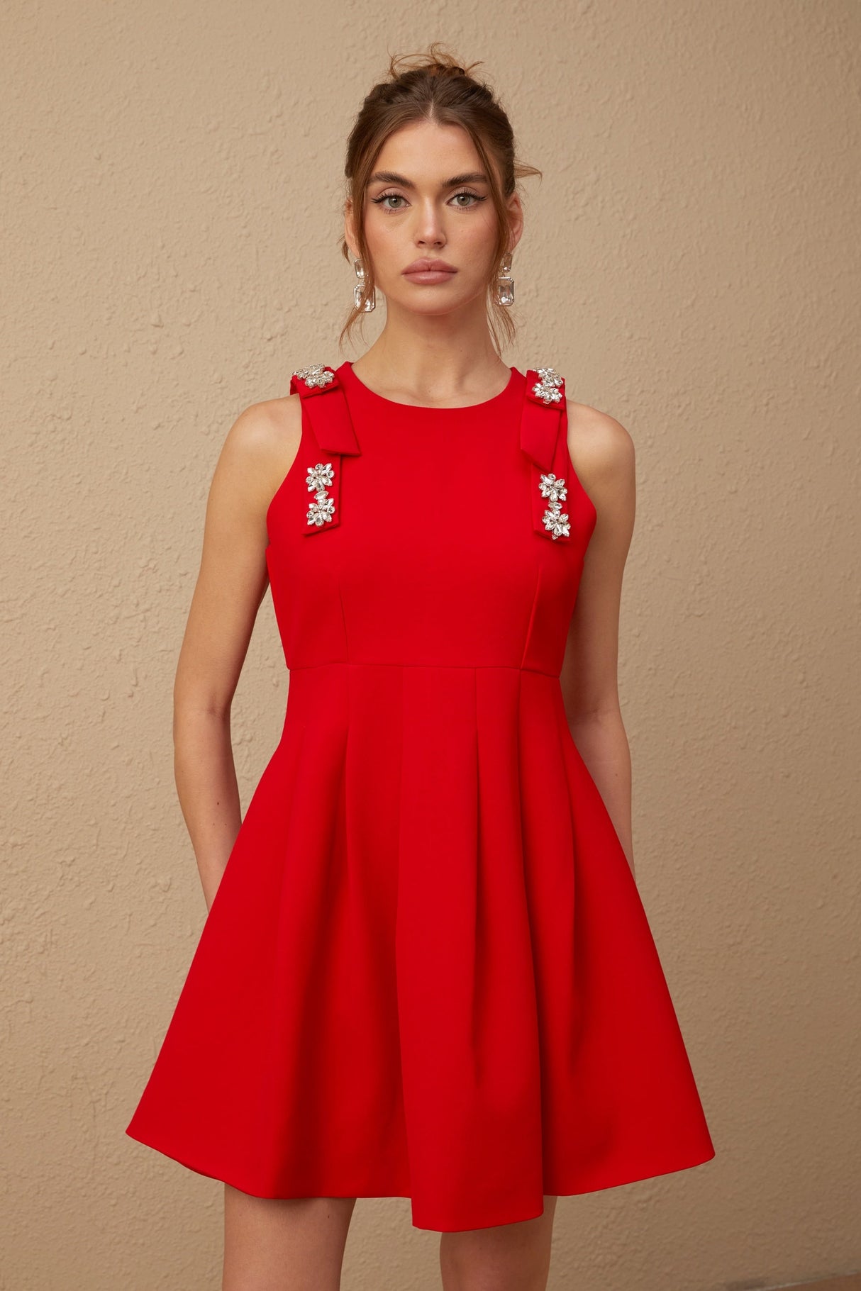 A young woman wearing a sleeveless red mini dress with a pleated skirt and a large bow detail at the neckline
