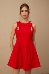 A young woman wearing a sleeveless red mini dress with a pleated skirt and a large bow detail at the neckline