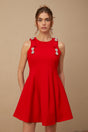 A young woman wearing a sleeveless red mini dress with a pleated skirt and a large bow detail at the neckline