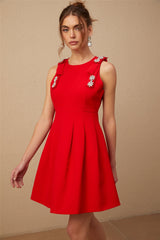 A young woman wearing a sleeveless red mini dress with a pleated skirt and a large bow detail at the neckline