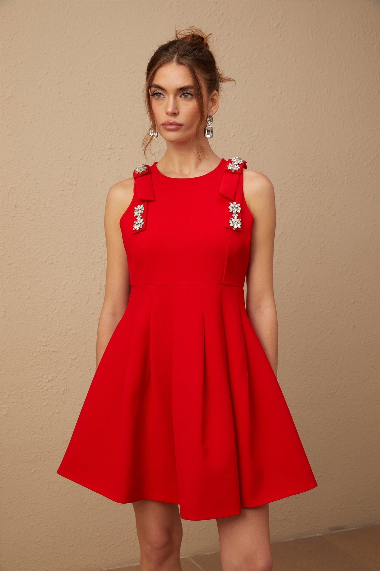 A young woman wearing a sleeveless red mini dress with a pleated skirt and a large bow detail at the waist