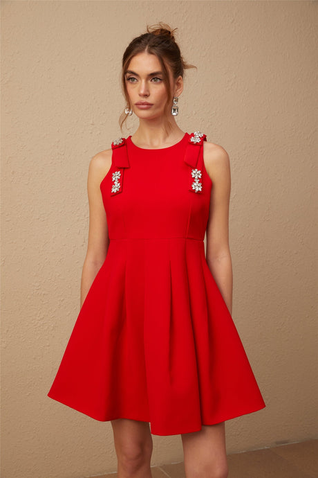 A young woman wearing a sleeveless red mini dress with a pleated skirt and a large bow detail at the waist