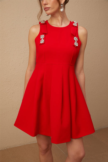 A young woman wearing a sleeveless red mini dress with a pleated skirt and a prominent bow detail at the front