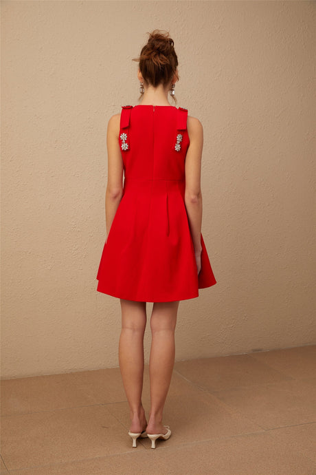 A young woman wearing a sleeveless red mini dress with a pleated skirt and a prominent bow detail at the waist