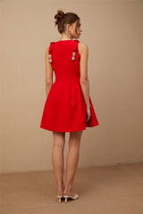 A young woman wearing a vibrant red sleeveless mini dress with a pleated skirt and a large bow detail at the neckline