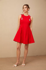 A young woman wearing a vibrant red sleeveless mini dress with a pleated skirt and a large bow detail at the waist