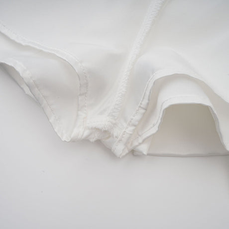 A young woman wearing a white halterneck mini dress with ruffled details standing against a plain background