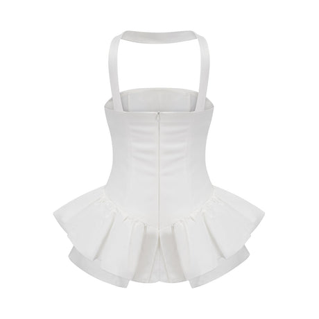 A young woman wearing a white halterneck mini dress with ruffled details standing against a plain background