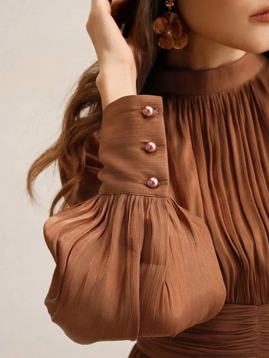 This elegant brown dress features soft, pleated fabric that drapes beautifully and creates a flattering silhouette. The.