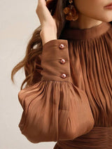 This elegant brown dress features soft, pleated fabric that drapes beautifully and creates a flattering silhouette. The.