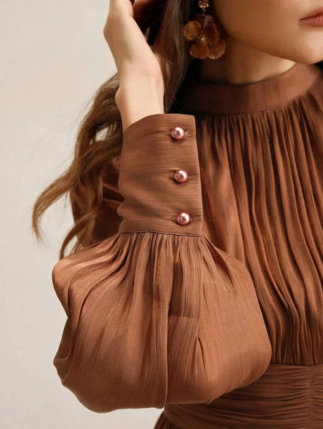 This elegant brown dress features soft, pleated fabric that drapes beautifully and creates a flattering silhouette. The.