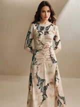This elegant long-sleeve dress features a soft, blush pink fabric adorned with delicate floral patterns and green leaves,.