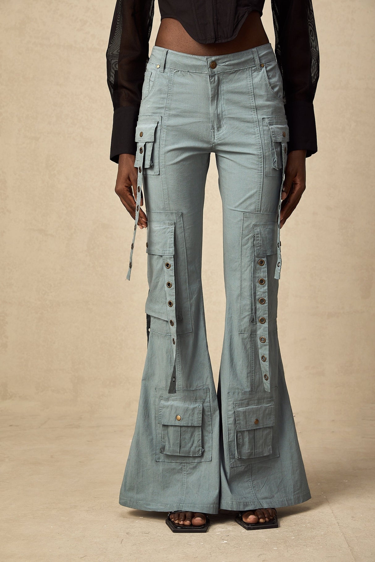 Beige flared cargo trousers with belt loops and multiple pockets worn by a model standing against a plain background