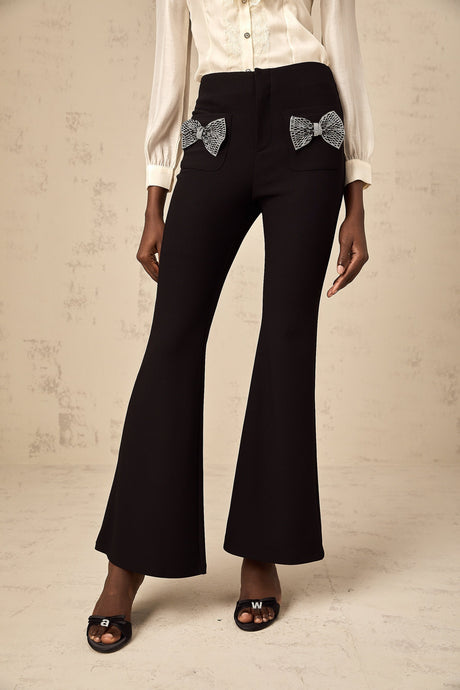 Black flared trousers with large decorative bow detail at waist