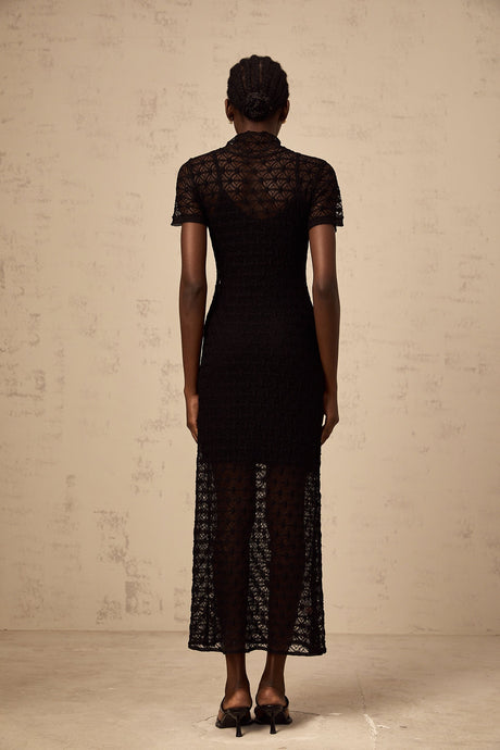 Black semi sheer knit midi dress worn by model standing against plain background