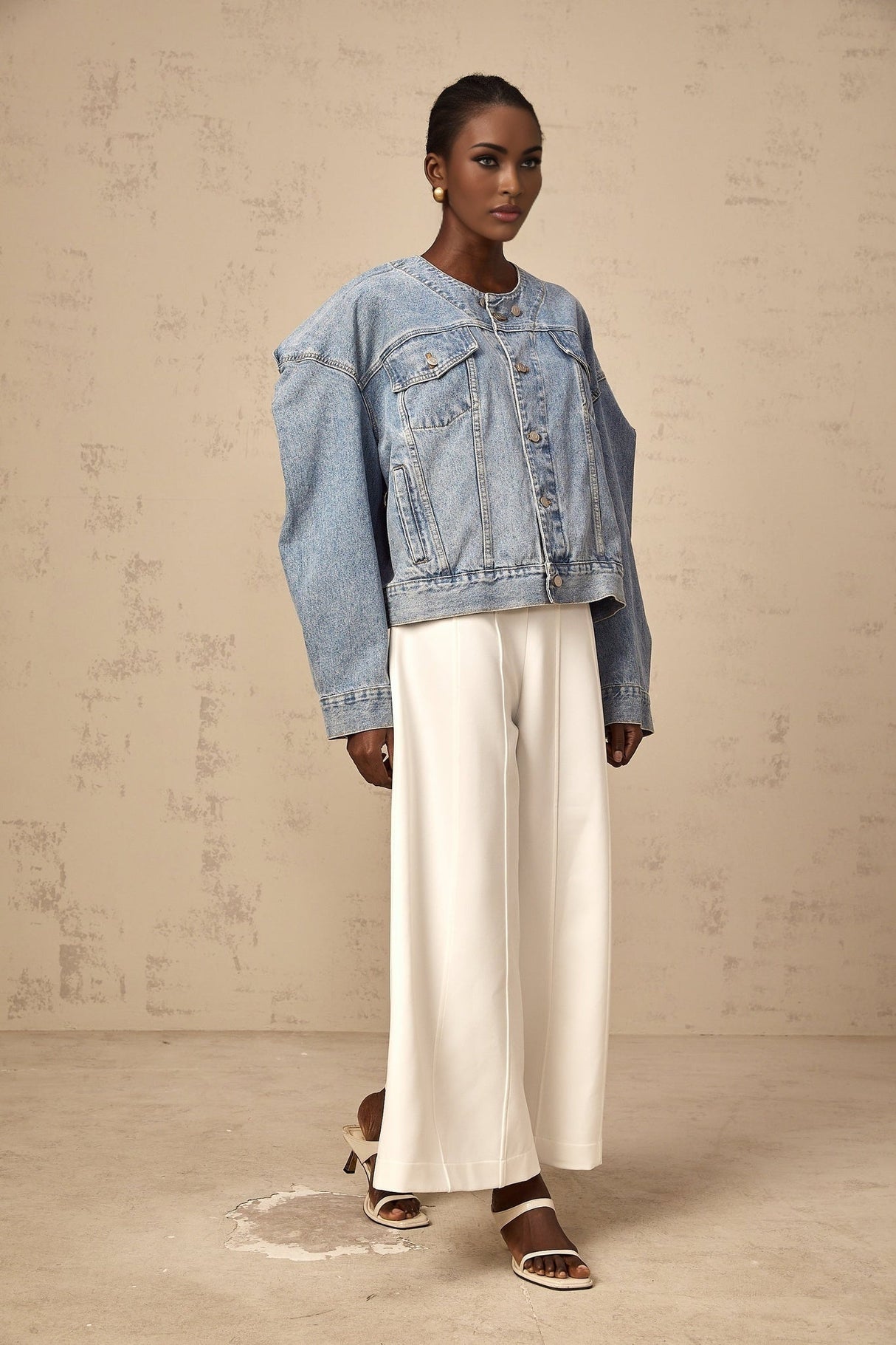 Blue collarless denim jacket worn by a woman standing against a plain background