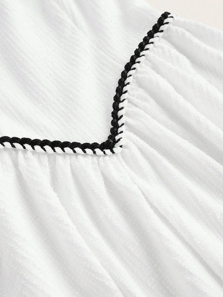 This charming white dress features delicate textured fabric with a playful black braided trim along the neckline, adding a.