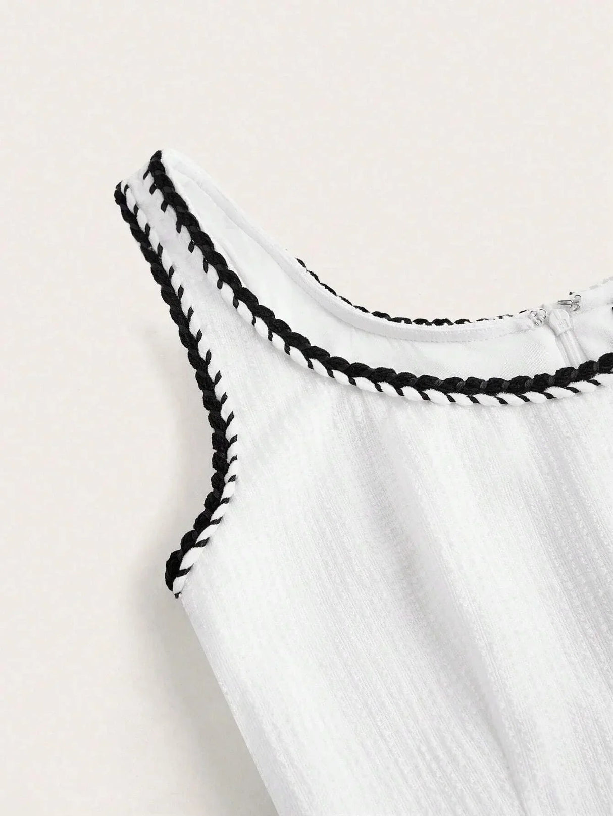 This elegant white dress features a flattering sleeveless design with a delicate black braided trim around the neckline,.