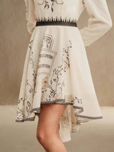 This elegant cream dress features delicate floral illustrations and a chic asymmetric hem, adding a playful touch to its.