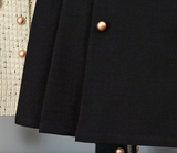 White tweed jacket with pearl buttons and contrasting cuffs, paired with a pleated black high-waisted skirt