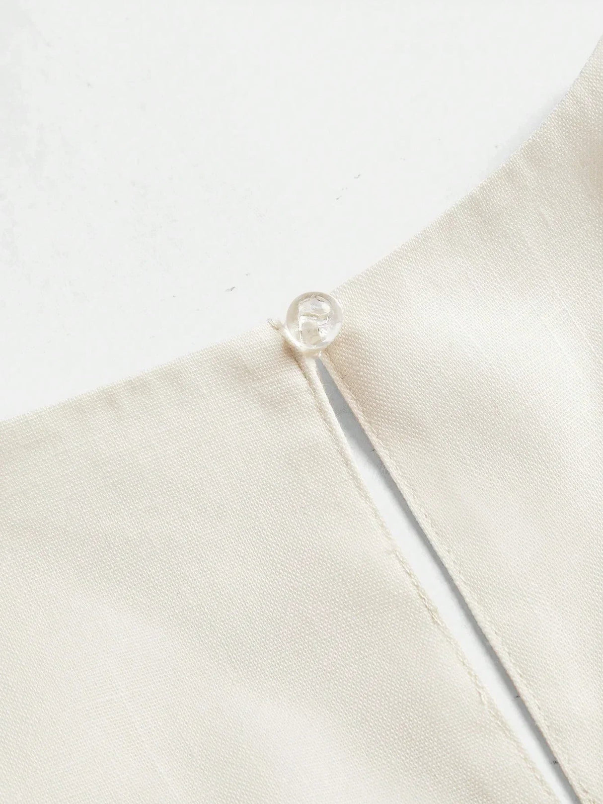 This elegant cream dress features a sleek, minimalist design with a delicate button detail at the neckline, crafted from a.
