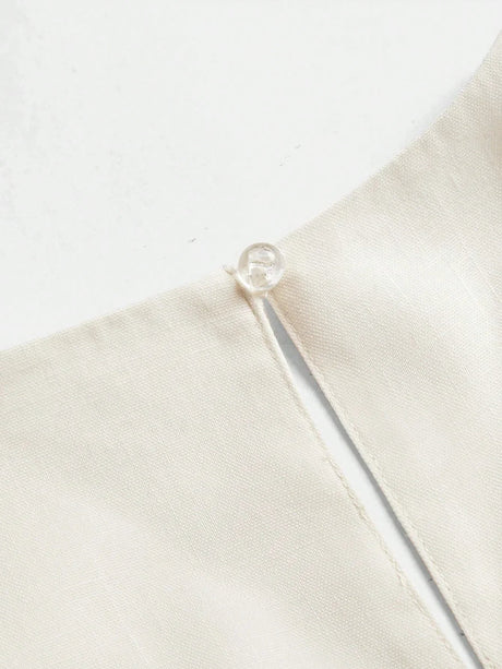 This elegant cream dress features a sleek, minimalist design with a delicate button detail at the neckline, crafted from a.