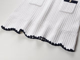 White knit cardigan with navy accents and gold buttons paired with a matching A-line skirt featuring a flared hem