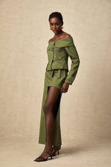 Green asymmetric jacket and matching skirt set worn by model standing against plain background