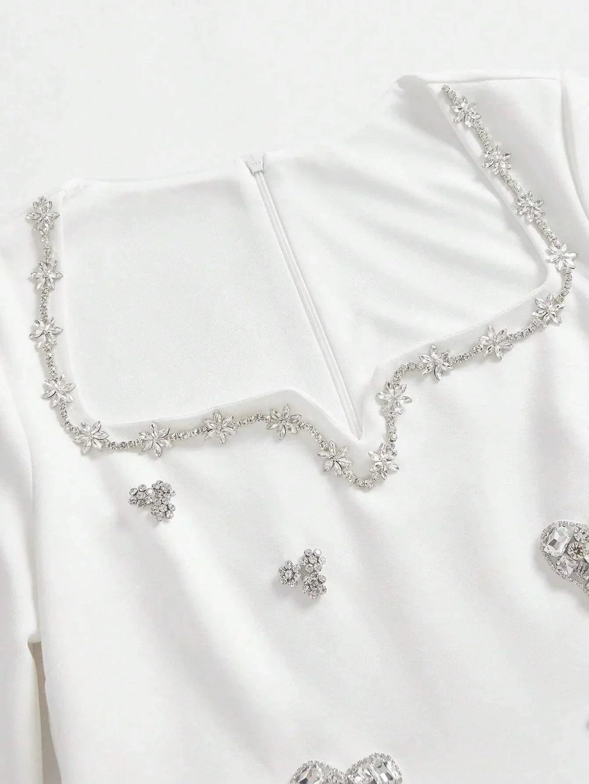This elegant white dress features a sophisticated square neckline adorned with delicate floral embellishments and shimmering.
