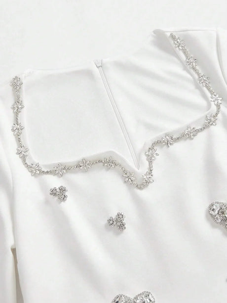 This elegant white dress features a sophisticated square neckline adorned with delicate floral embellishments and shimmering.