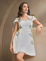 This elegant white dress features delicate floral embroidery in soft blue and yellow shades, creating a fresh and whimsical.