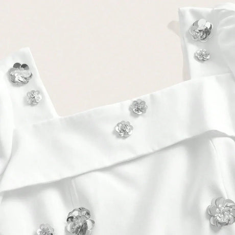 This elegant white dress features delicate silver flower embellishments that add a touch of glamour to its chic design. The.