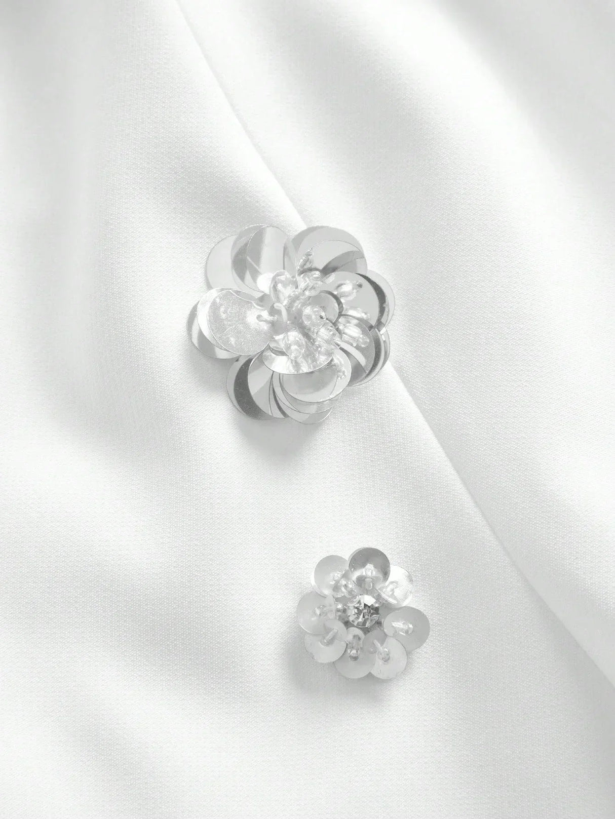 Delicate silver floral embellishments adorn a smooth white fabric, adding an elegant touch to this sophisticated dress. The.