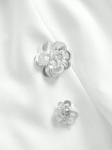 Delicate silver floral embellishments adorn a smooth white fabric, adding an elegant touch to this sophisticated dress. The.