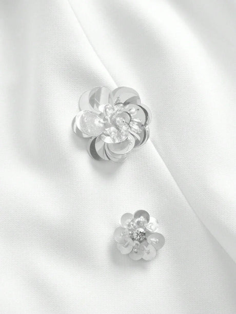 Delicate silver floral embellishments adorn a smooth white fabric, adding an elegant touch to this sophisticated dress. The.