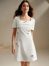 Elevate your wardrobe with this charming white mini dress, featuring a square neckline and short sleeves adorned with.