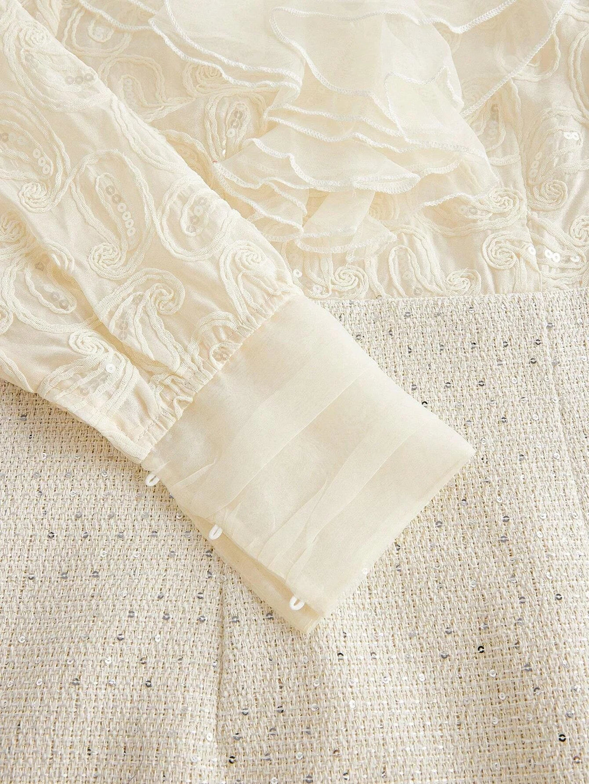 This elegant cream dress features intricate pastel embroidery and delicate flowing ruffles, creating a romantic and.
