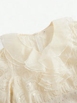 This elegant cream-colored dress features a playful ruffled collar and delicate, swirling embroidery accented with subtle.