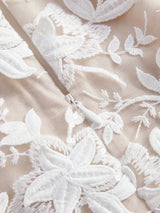 This elegant dress features a soft beige fabric adorned with intricate white floral embroidery, creating a delicate and.