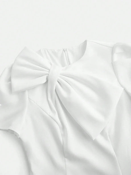 This elegant white dress features a sophisticated bow detail at the neckline, crafted from lightweight, flowing fabric that.